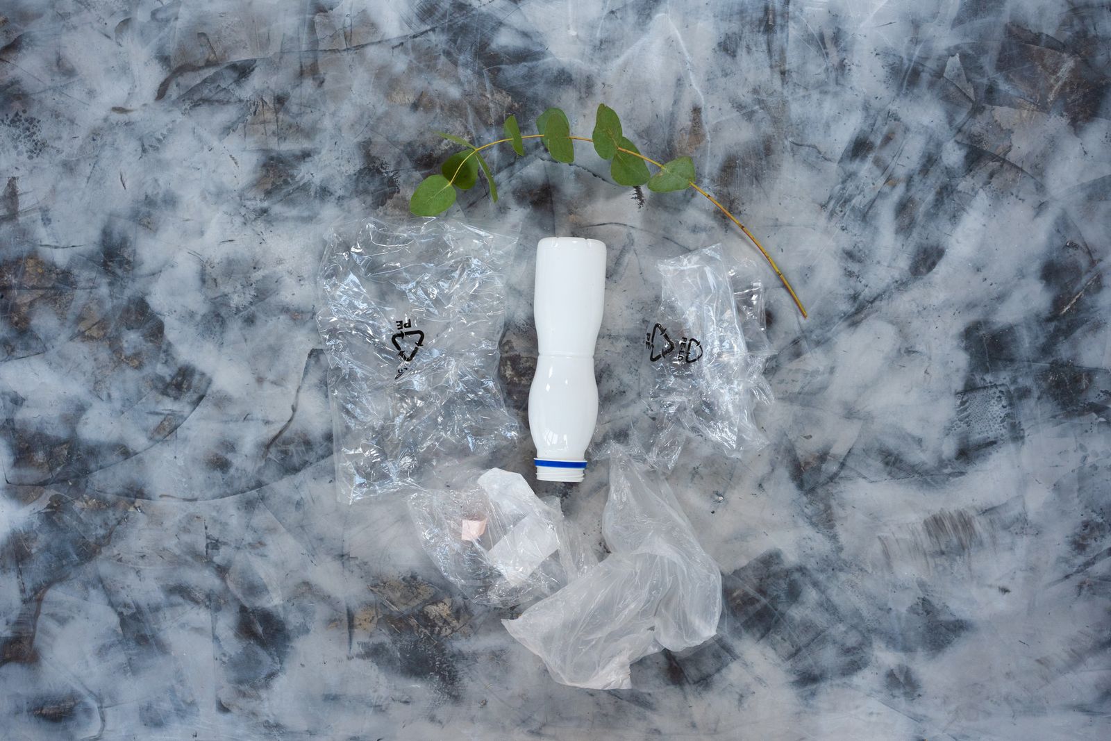 Nature morte conceptuelle de déchets plastiques et d'une feuille, symbolisant la pollution.